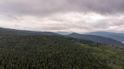 Fototapeta premium Majestic Mountains, Lush Green Forests, And Dramatic Clouds With The Sun Casting A Golden Glow. Aerial View Capturing The Stunning Beauty Of Nature From A Bird’s-Eye Perspective. 