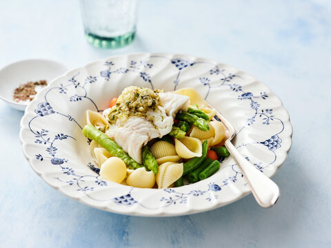 A plated dish features tender pasta shells topped with cooked fish and vibrant green asparagus, presenting an inviting and colorful meal perfect for lunch or dinner
