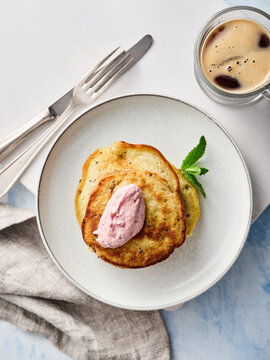 Pancakes are plated beautifully with a dollop of flavored cream on top, accompanied by a glass of iced coffee. A mint leaf adds a touch of freshness to the presentation