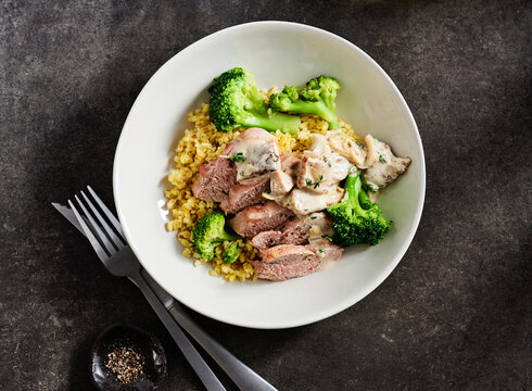 Tender pork is sliced and served on a bowl of fluffy bulgur wheat, accompanied by vibrant steamed broccoli and a rich creamy sauce. Perfect for a healthy meal