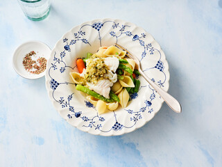 A beautifully arranged bowl features cod fish pasta topped with fresh vegetables, highlighting a culinary delight. The setting is complemented by a delicate tableware design