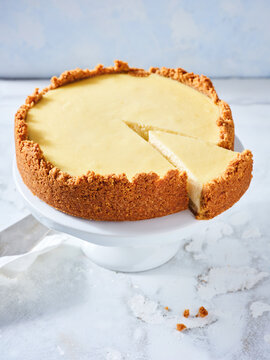 This delicious cheesecake is displayed on a white cake stand, showcasing its creamy filling and crumbly crust. A slice has been cut, revealing the dessert's luscious texture, perfect for sharing