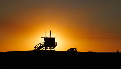 Los Angeles beach at sunset, featuring a lifeguard tower silhouette against a glowing orange and purple horizon