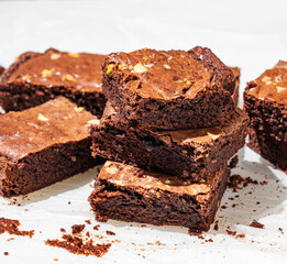 Chocolate brownie with nuts cut into pieces on baking paper close-up with morning light.