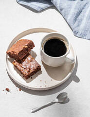 Pieces of chocolate brownie with nuts on a plate with a cup of espresso coffee on a light background