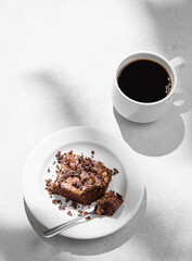 Pieces of chocolate brownie with nuts on a plate with a cup of espresso coffee on a light background