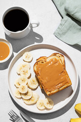 Peanut butter toast on a plate with banana on a light background with a cup of freshly brewed coffee