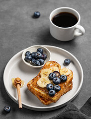 Peanut butter toast with banana, blueberry and honey on a plate on a dark  background