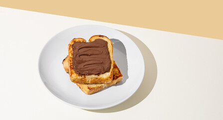 Toasted bread with chocolate cream on a white plate on a light  background with shadow.