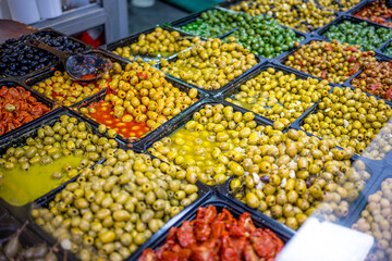 A vibrant market display of various marinated green and yellow olives in trays, seasoned and colorful