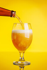 A frothy glass of fresh beer against a bright yellow background