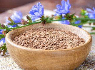 Ground chicory root in a wooden cup and chicory flowers on a rustic wooden background. Alternative medicine. Healthy drinks. chicory drink