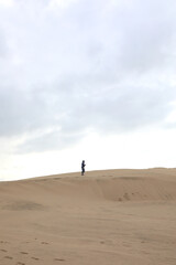person walking on sand of a desert dune with the sky and clouds above
