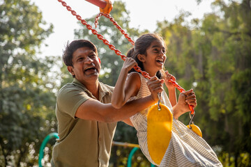Indian happy father pushes swings with his Cute Little Daughter at park