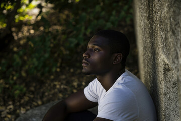 Fototapeta premium sad African-American man in a white shirt sitting near a stone , zero discrimination day
