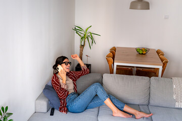A Latin woman sitting on a couch in a bright living room, smiling as she talks on her phone....