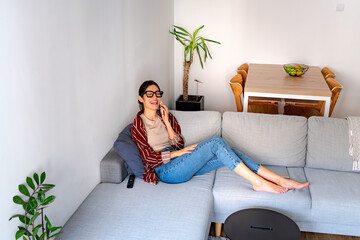 A Latin woman sitting on a couch in a bright living room, smiling as she talks on her phone....