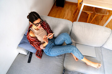 Hight angle view of a woman on the sofa with her phone, scrolling through content in a sunlit...
