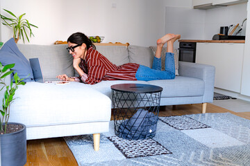 A woman on a couch, looking at her phone in a bright and cheerful living room.