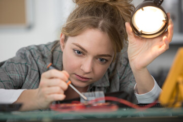young female electronic engineer soldering computer motherboard in laboratory