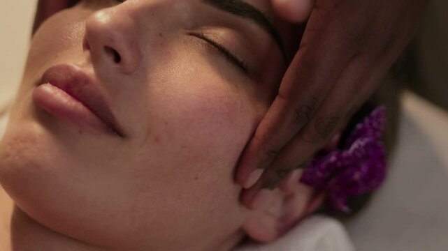 Close-up view of face of young woman enjoying sculpting cheekbone massage when lying with eyes closed during session