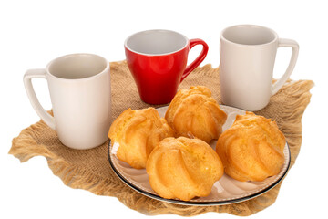 Four eclairs on a ceramic saucer with cups of coffee with a jute napkin on a white background, close-up.