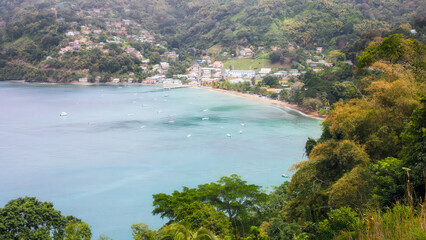 View from above to Charlotteville seaside village with colorful houses, boats in the bay, surrounding rainforest groved hills. Tropical destination in Tobago, Trinidad and Tobago.