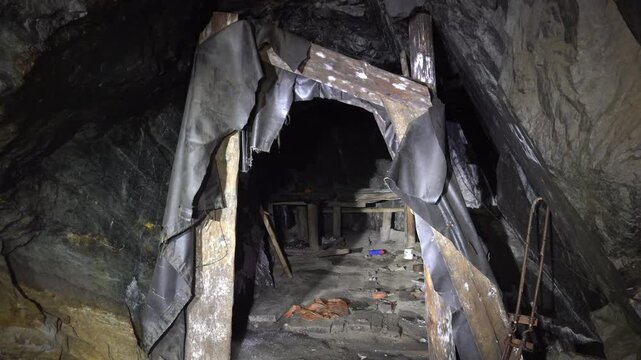An abandoned dirty room inside the mine. Piles are standing trampling stones so that the ceiling does not collapse, garbage is lying around. High humidity on stone walls. The torn material is hanging
