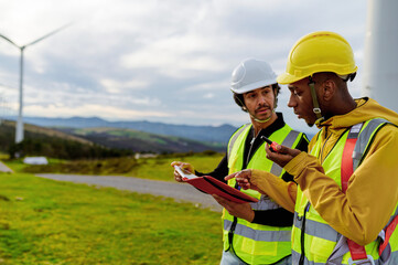 Two workers analyzing data using a digital tablet and walkie talkie in a wind turbine park, working on renewable energy development