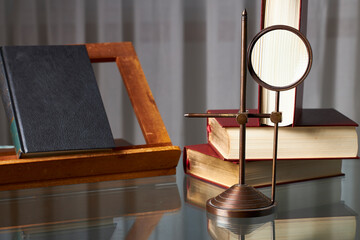 Magnifying glass and books. An old rotating magnifying glass on a glass surface and some old books
