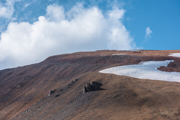 Rock and snowfield on mountainside in changeable weather. Sunlit stony mountain range with snow...