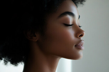 Fototapeta premium Woman with natural afro hairstyle poses calmly in a softly lit room, showcasing her profile and serene expression