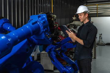 Young male robotic engineer working with automictic robotic arm in robot factory