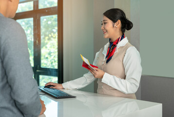 Smiling flight attendant working at check-in desk in airport. Female airline staff checking passport of male traveler..