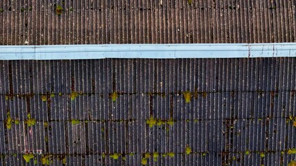 Aerial view of an old corrugated roof featuring moss growth, dirt, and a light blue pipe running horizontally across. - Powered by Adobe
