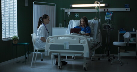 Fototapeta premium Doctor seated beside elderly patient, providing document for her to sign.
