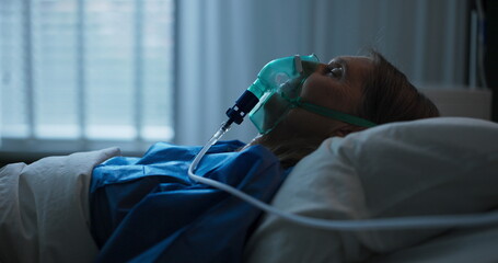 Elderly lady in a hospital bed wearing an oxygen mask, receiving treatment for lung problems.