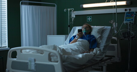 Aged patient in bed, watching funny videos on her phone, the oxygen mask a constant companion...