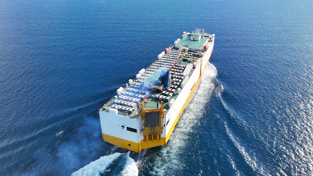 Aerial drone tracking photo of roll on roll off or ro ro cargo ship with deck designed to carry wheeled cargo cruising outside popular Mediterranean port with deep blue sea