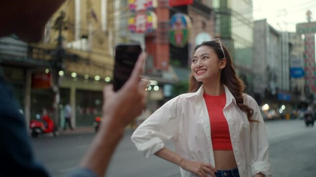 Happy young asian traveler couple taking photo girlfriend using smartphone while standing in famous china town bangkok street in Thailand, two people capturing memories adventure together.

