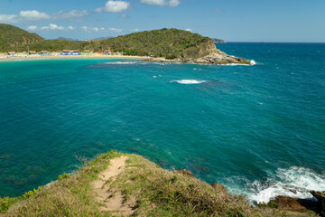 View from the top of a mountain, with rocks, lots of vegetation and mountains in the background and blue sky and crystal clear waters on the Conchas beaches, Cabo Frio region, Rio de Janeiro, Brazil.
