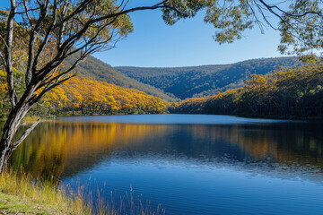 Obraz premium Beautiful Scenic Lake Surrounded by Autumn Trees and Lush Green Hills