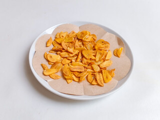 Fried garlic chips or slice on white plate. Use as condiment topping in various Indonesian culinary meal.