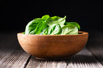 Young baby spinach leaves in a wooden bowl on rustic wooden table. Food photography