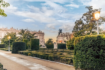 Fototapeta premium The lush gardens of Plaza de Oriente in Madrid, Spain, with the equestrian statue of King Philip IV in the distance. The beautifully trimmed hedges and evening light create a serene atmosphere