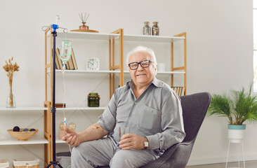 Portrait of a senior happy smiling man sitting on chair in medical clinic or at home receiving IV...