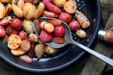 Fried radishes with herbs and spices on an iron frying pan with a spoon. Vegetarian food