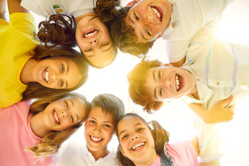 Childhood. Portrait of happy preteen children standing in circle, hugging each other and smiling at camera. Smiling faces of little friends standing with arms around and looking down to camera.
