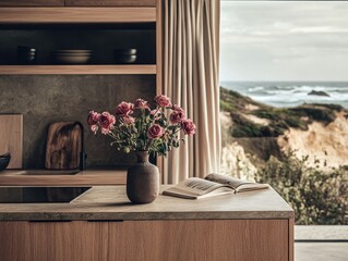 A vase of flowers sits on a counter next to a book. The vase is brown and the flowers are pink