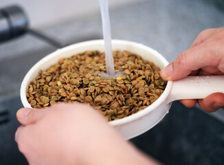 A woman rinsing green lentils in a sieve. Close up.